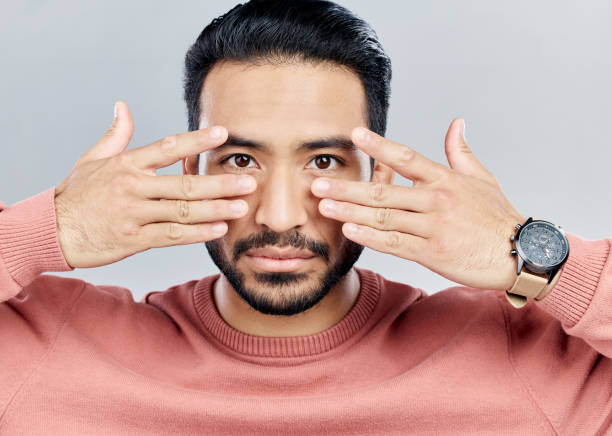 istock Portrait, eyes and vision with a man in studio on a gray background making a masquerade hand gesture. Face, hands and focus with a handsome young male posing against a wall while touching his cheeks 1496345385