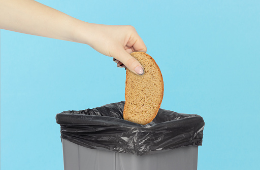 throwing a piece of bread into the trash can, bread in hand in front of the trash can, stale food concept. rejection of flour products