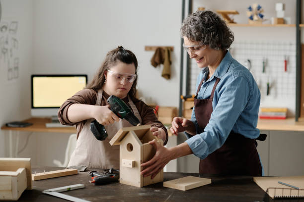 Girl with down syndrome making birdhouse Girl with down syndrome using drill to make birdhouse together with master in workshop drill team stock pictures, royalty-free photos & images