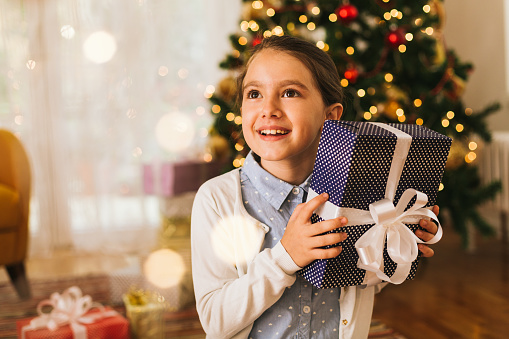Excited little girl holding Christmas present that she is about to open on a Christmas morning