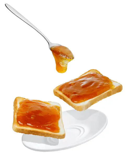 apricot jam pouring from spoon on bread toasts in saucer isolated on white background