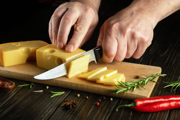 istock Hands of a cook with a knife cut cheese on a cutting board before preparing pizza. Dark space for recipe 1496352185