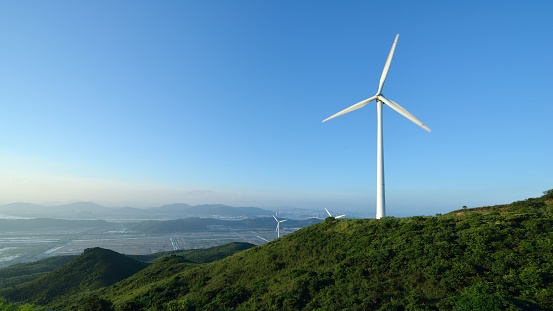 The white wind turbines atop a mountain peak with a bright blue sky in the background