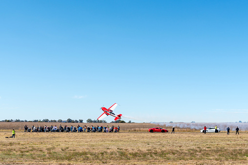 Bloemfontein, South Africa - May 20, 2023: Sideways flyby next to a display of Harley Davidson motorcycles and cars at the Tempe Airport in Bloemfontein. People are visible