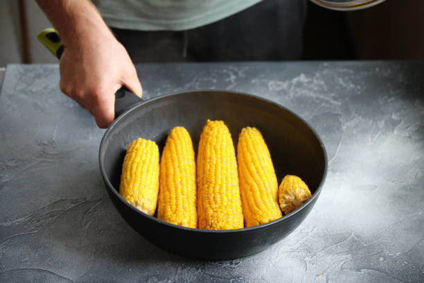 un uomo che tiene una padella con orecchie di mais arrostite. mangiare sano. - corn on the cob corn cooked boiled foto e immagini stock