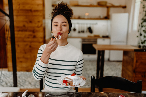 Young woman eating slice of strawberry cake at home