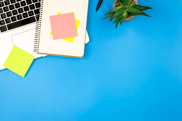istock Laptop, notepad and paper reminders on blue background, flat lay. 1496361540