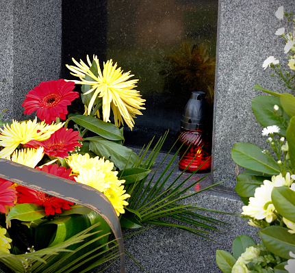 Close up of burning candle and fresh floral decoration on the grave after a funeral. Funeral decoration at the cemetery in the Czech Republic. Last good bye concept. Rest in peace concept.