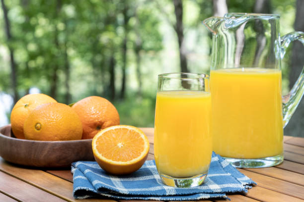 Glass of orange juice and oranges outdoors on a wooden table with nature background