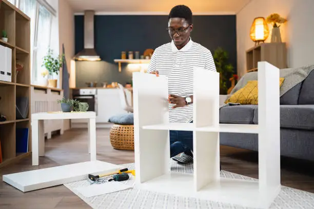 Young African-American man assembling new furniture at his modern apartment