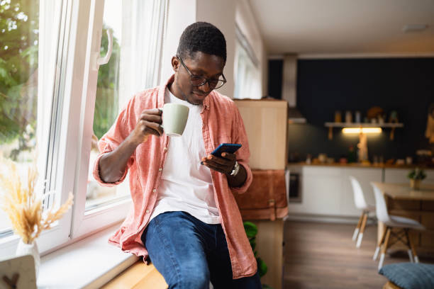 istock African-American man siting by the window while holding cup of coffee and using mobile phone 1496370887