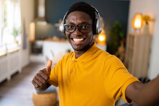 At his apartment, a young African-American man, taking selfie while listening to music on wireless headphones