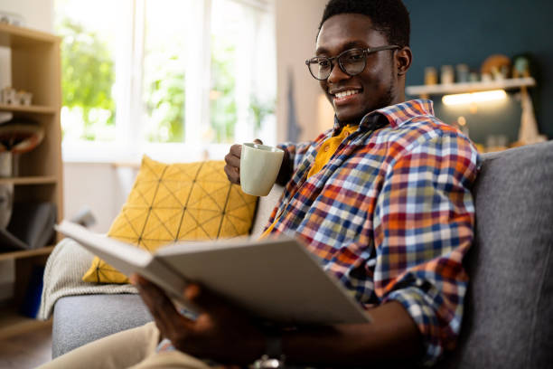 istock African-American man drinking coffee and reading a book, while sitting on the sofa 1496371376