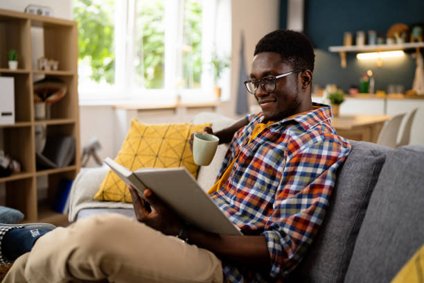 istock African-American man drinking coffee and reading a book, while sitting on the sofa 1496371513