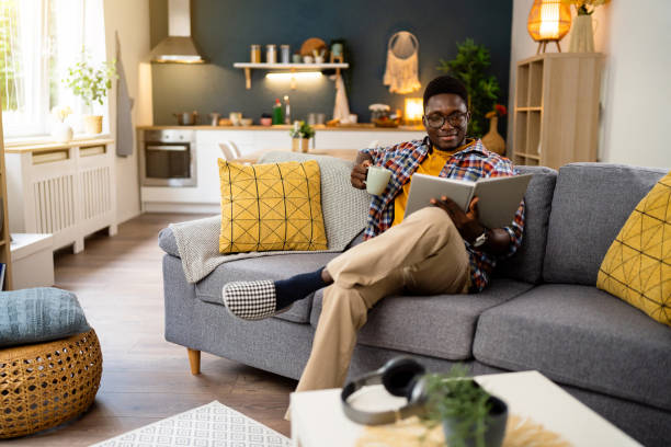 istock African-American man drinking coffee and reading a book, while sitting on the sofa 1496371516