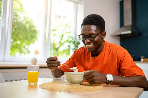 Young man of African-American ethnicity, sitting for a dining table and eating oatmeal for breakfast