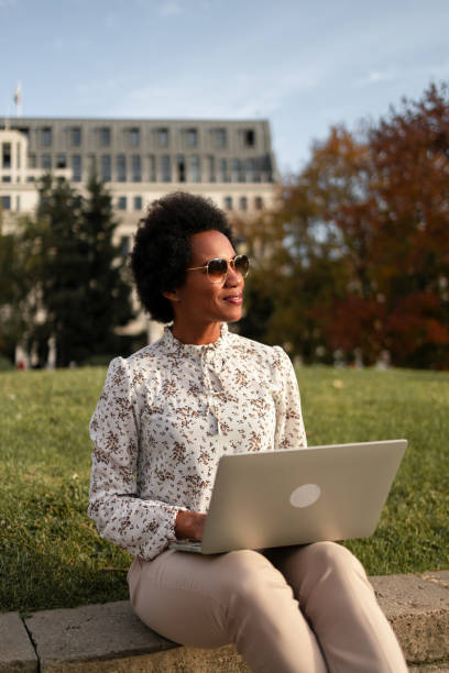 istock African female looking on the side while working over the laptop, being outdoors, sitting at the park. 1496372904