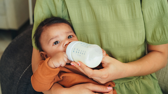 Mother feeding baby boy with infant formula in baby bottle