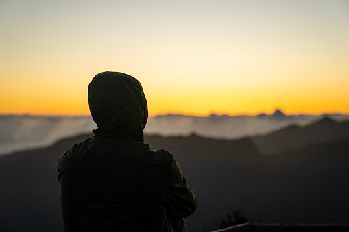 Person standing back to camera observing the setting sun on mountain summit in Madeira