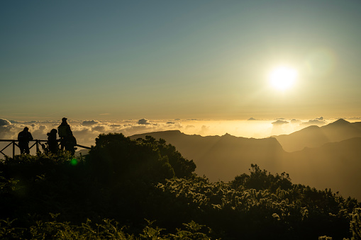 People standing back to camera taking pictures of setting sun on mountain summit in Madeira