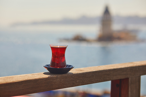 Turkish glass in form of a tulip filled with hot black tea with view to Maiden's Tower in Uskudar district on Asian side of Istanbul, Turkey