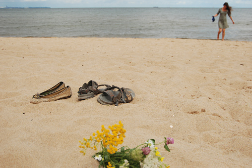 Flowers and shoes on the sand. Girl near the sea on the horizon.