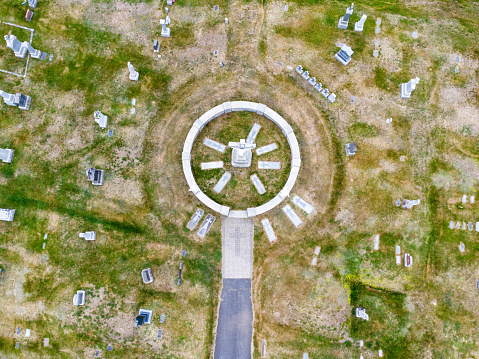 Aerial view of cemetery with rows of tombstones, footpath and grass during day of springtime in Coaticook, Quebec.
There is a circle with a statue of Jesus on the cross.