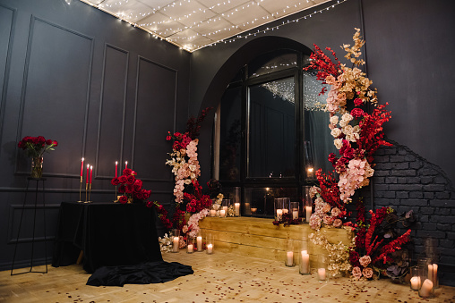 Romantic date in restaurant. Luxury candlelight dinner setup table for couple on Valentine's day. Location with arch, wall, photozone decoration flowers, decor candles for surprise marriage proposal.