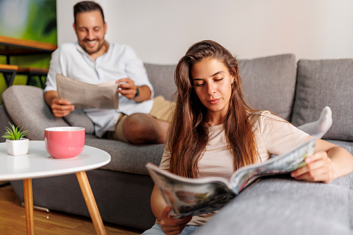 Beautiful couple reading newspaper and drinking coffee while spending leisure time together at home in the morning
