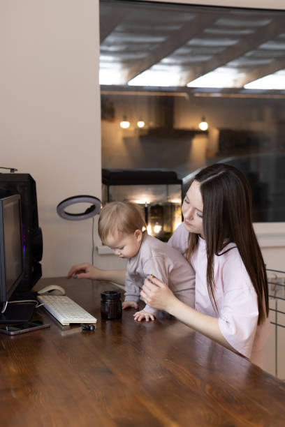 istock A young mother with a baby in her arms works on a computer at home remotely 1496394592