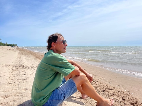 Profile view of Senior man with sun glasses sits on Lake Michigan beach in Two Rivers.