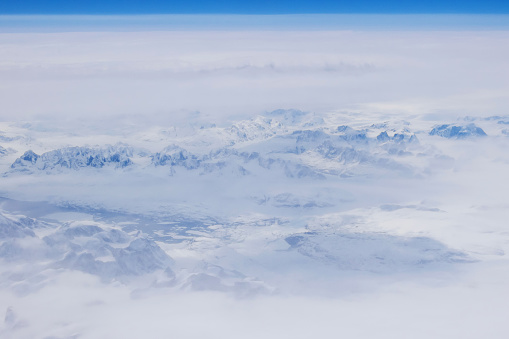 Beautiful high snow covered mountain peaks of Greenland create breathtaking landscape in clouds