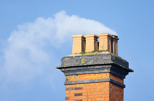 Wood smoke against a blue sky billowing from a brick chimney of an old UK house
