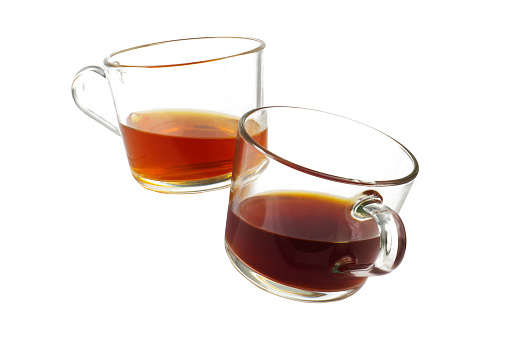 Two transparent glass coffee cups clinking and flying in a toast in the air, one dark roasted coffee and one light roasted coffee next to each other, studio shot isolated on white background