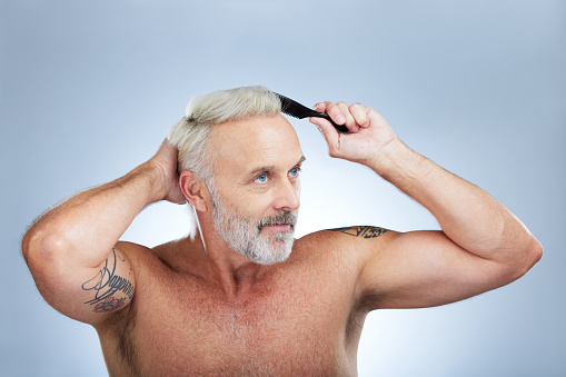 Mature man, brush hair and scalp health treatment in a studio with a model doing beauty routine. Wellness lifestyle, hairstyle care and male with hairdresser comb with an isolated grey background