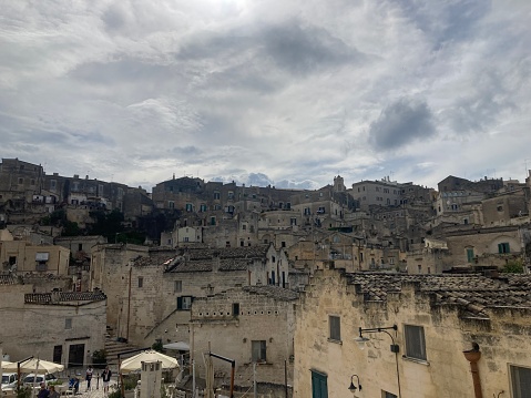 An idyllic cityscape of the old town of Matera, in southern Italy, known worldwide as 'Sassi di Matera' (Matera's Stones). At the center stands the majestic facade and the bell tower of the Duomo, or Cathedral of the Madonna della Bruna and of Sant'Eustachio, built in the Apulian Romanesque style in the 13th century. The ancient city of Matera, in the region of Basilicata, is one of the oldest urban settlements in the world, with a human presence that dates back to more than 9,000 years ago, in the Paleolithic period. The Matera settlement stands on two rocky limestone hills called 'Sassi' (Sasso Caveoso and Sasso Barisano), where the first human communities lived in the caves of the area. The rock cavities have served over the centuries as a primitive dwelling, foundations and material for the construction of houses, roads and beautiful churches, making Matera a unique city in the world. In 1993 the Sassi of Matera were declared a World Heritage Site by Unesco. Super wide angle image in 16:9 and High Definition format.