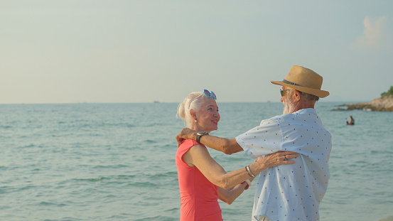 Two elderly men and women dancing at the beach on their summer vacation and they smile and enjoy their day off.