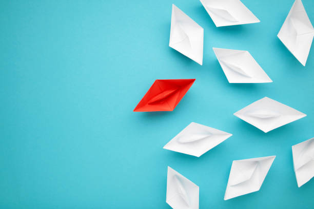 istock Leadership concept. Red leader paper ship leading among white on blue background. 1496411440