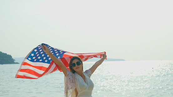 young women hold American flags on the beach and the sea on their summer vacation and they smile and enjoy their vacation.
