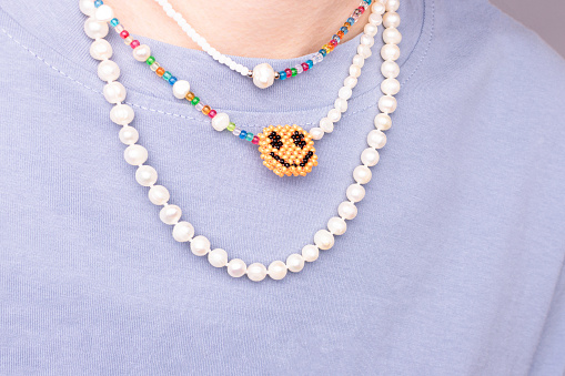 Multicolored pearl beads on a woman in a t-shirt in front of blue background. Selective focus.