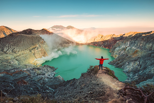 Successful traveler man standing on the crater of Kawah Ijen volcano with sunrise sky in the morning at East Java, Indonesia