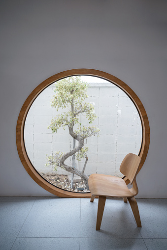 Minimalism interior of wooden chair with round window and tree at patio