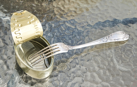 Open empty tin can and fork on the glass table surface