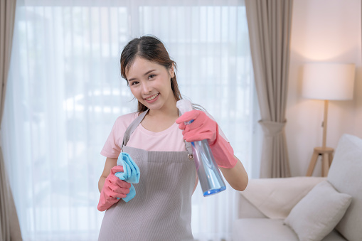 Happy Asian woman cleaning the living room at home with cleaning supplies.