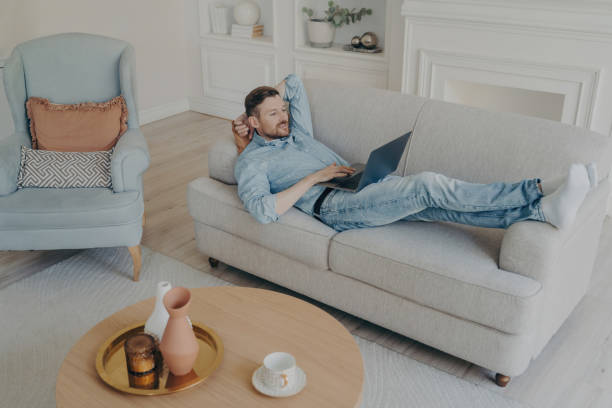 istock Young businessman working remotely at home while lying on couch 1496418031