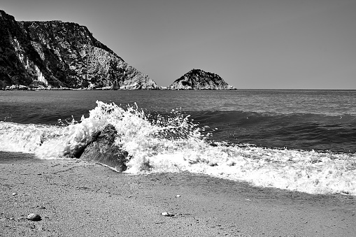 foaming waves, and boulders on a pebble beach of Petani Bay on the island of Kefalonia in Greece,  monochrome