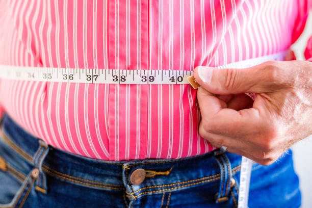 istock Overweight man measuring waist using tape measure 1496423130