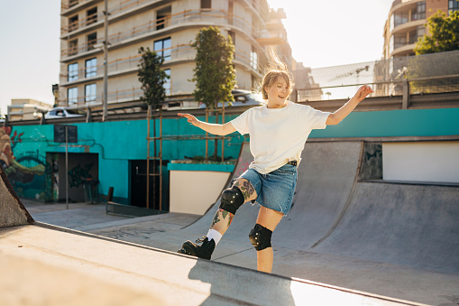 Concentrated young woman performs various jumps and exhibitions with roller skates in a skate park