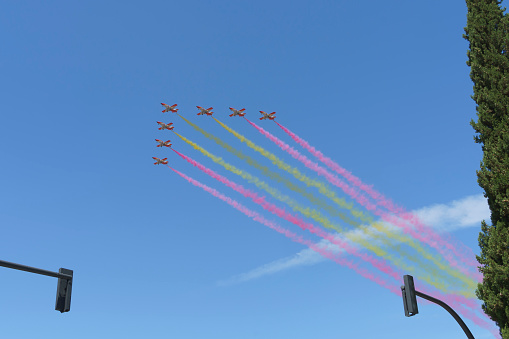 Granada, Spain; June 03 - 2023: Aircraft in formation leave red and yellow smoke trails in the blue sky on the day of the Spanish Armed Forces.