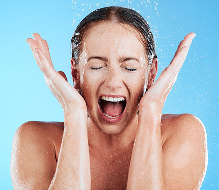 Shower, water and excited woman in a studio feeling happy from cleaning and skincare. Wellness, splash and beauty routine of a female model with facial dermatology and self care with blue background